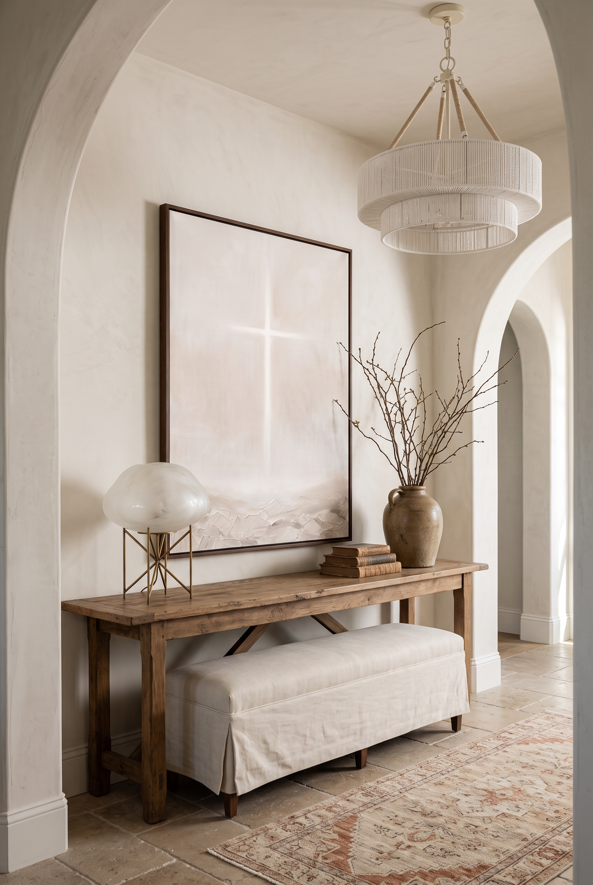 The Cross framed canvas above an antique console in an arched plaster entry with a woven chandelier